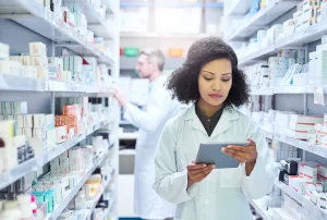 Woman, pharmacy and tablet with reading for inventory, stock or drugs for order from supplier. Pharmacist, people and notes on touchscreen for sales stats, product or pills on healthcare app at shop.